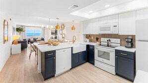 Una cocina moderna con muebles blancos y oscuros, una isla central y vistas al exterior.