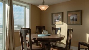 A dining room with a round table, four chairs, a hanging light fixture, and two framed pictures on the wall.
