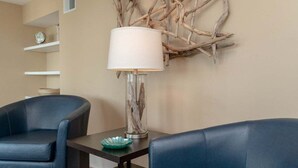 A room with two blue leather chairs, a small table with a lamp, and a wall-mounted decorative piece.
