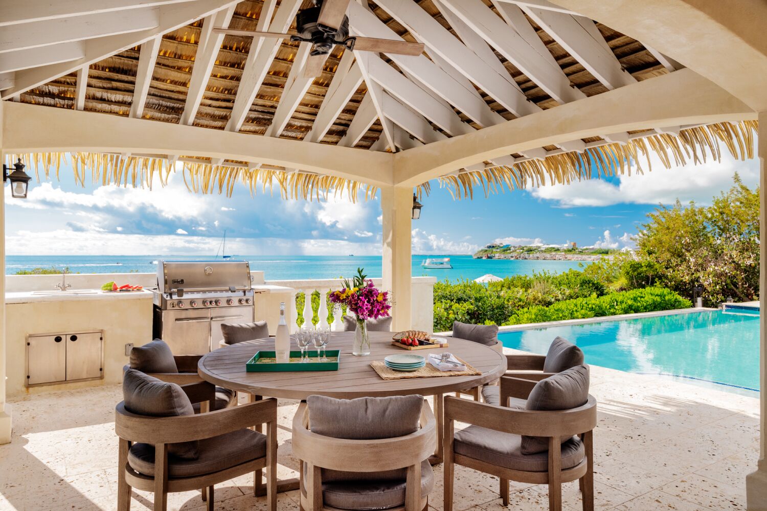 A covered outdoor dining area with a grill, seating, and a view of the ocean.