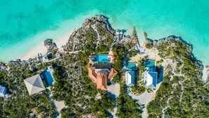 Vue aérienne d’un complexe hôtelier comprenant plusieurs bâtiments, une piscine centrale et une zone de plage.