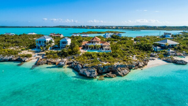 Vue aérienne d’une station balnéaire comprenant plusieurs villas, des eaux turquoise et limpides, et une végétation luxuriante.