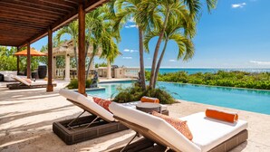 Un espace aménagé au bord de la piscine, avec des chaises longues, un coin salon abrité et une vue sur l’océan.