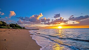 Ein Strand bei Sonnenuntergang, Wellen und bewölktem Himmel.