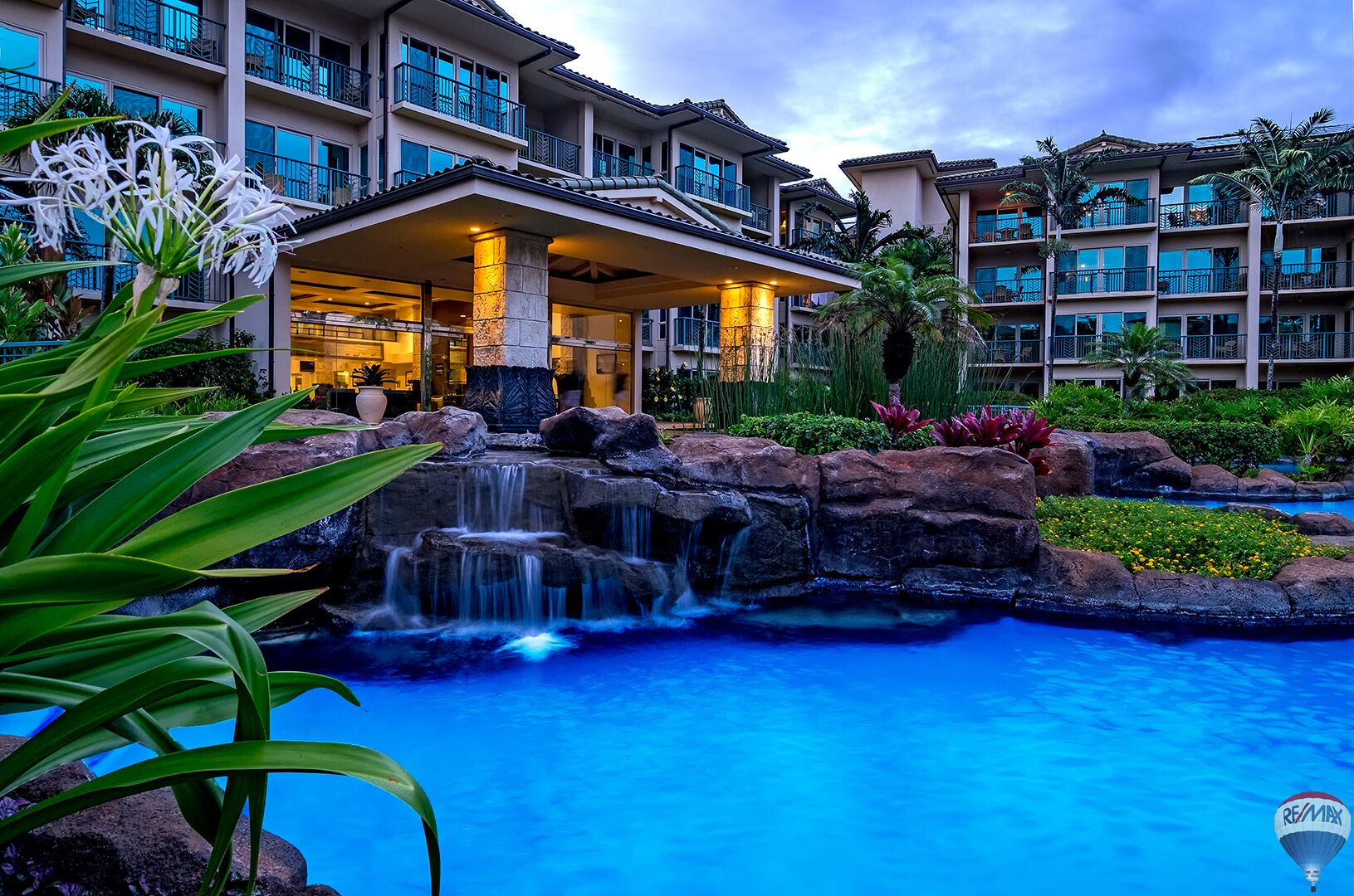 A hotel with a pool, waterfall, and lush landscaping.