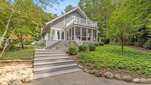 Une maison à deux étages dotée d’un porche abrité, d’un escalier menant à l’entrée et d’un jardin bien entretenu avec diverses plantes et une pelouse.