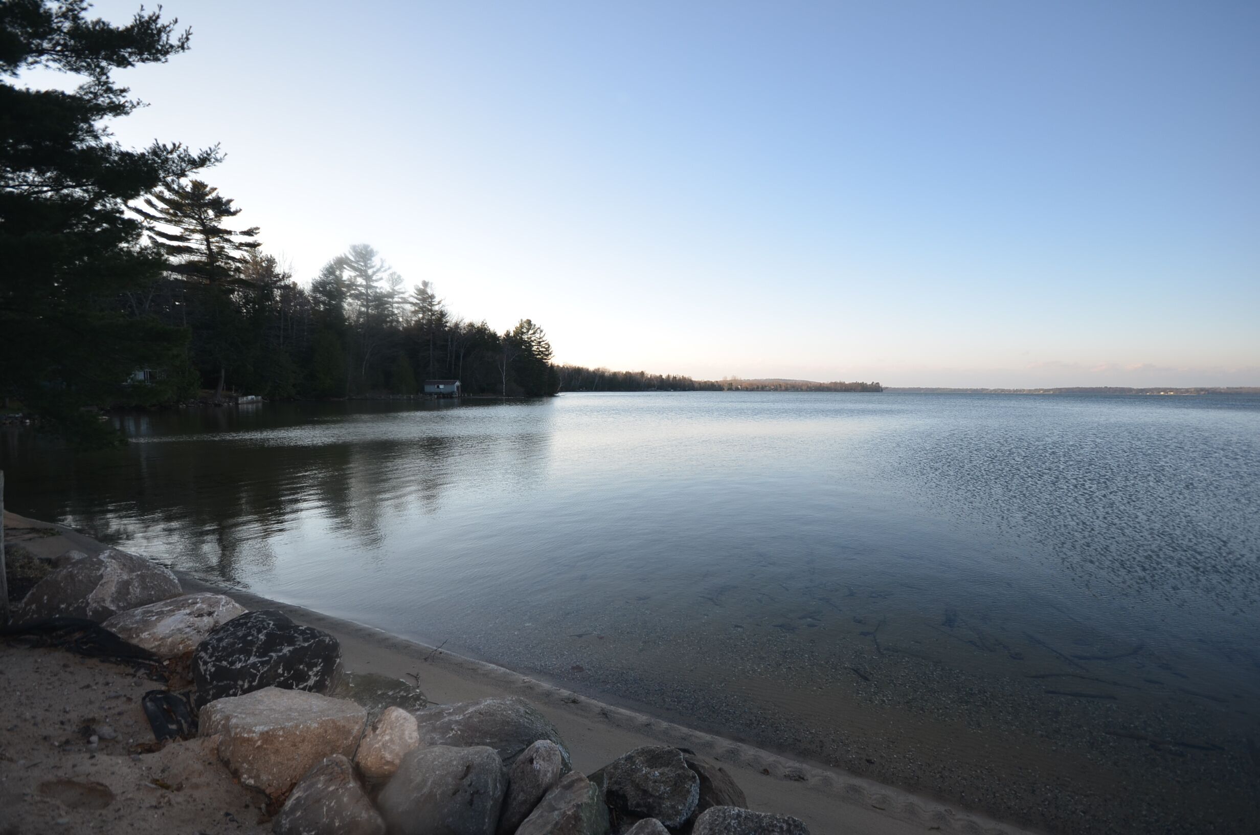 A calm lake with a rocky shoreline and trees in the background.