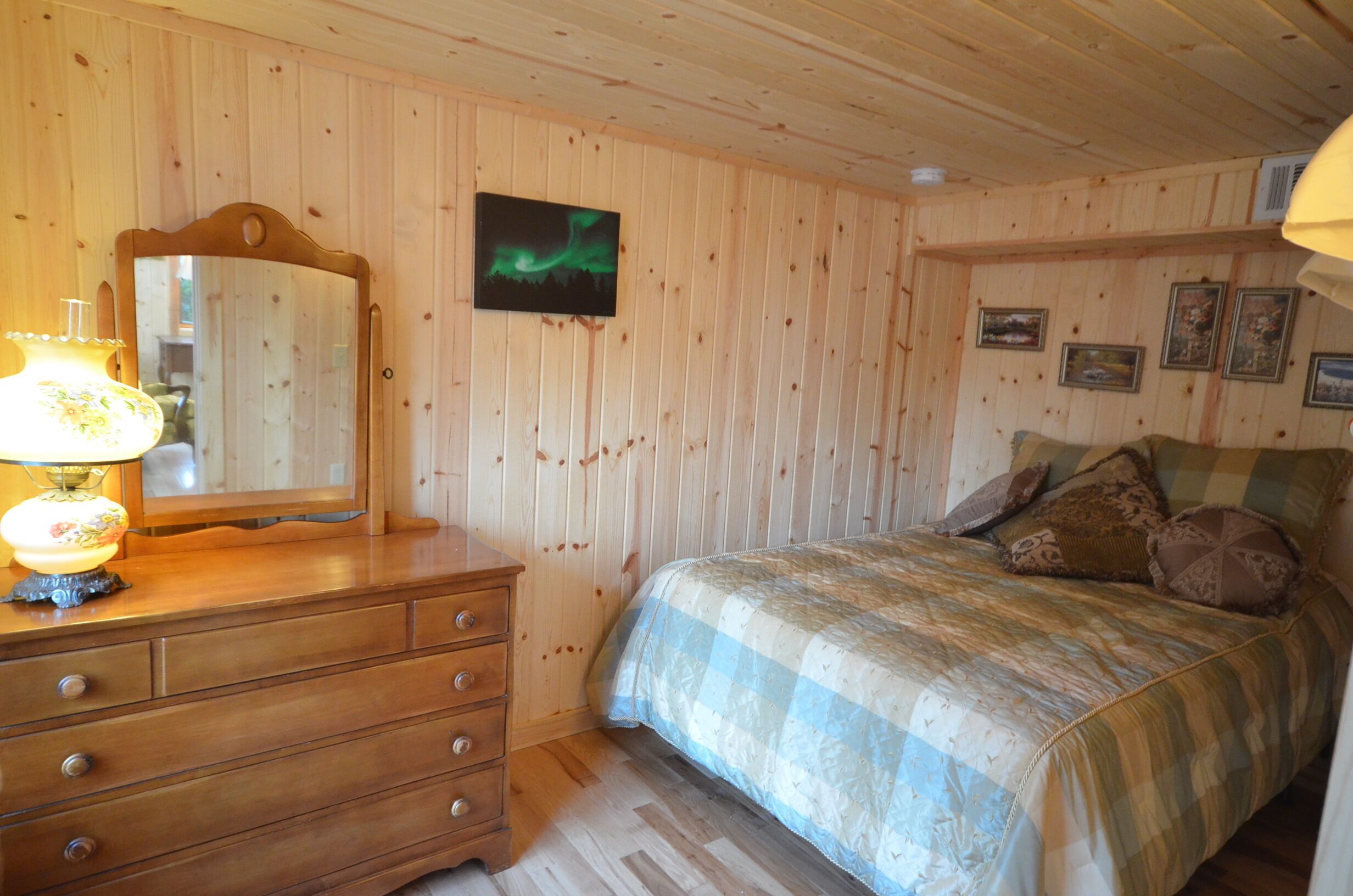 A wooden-paneled room with a bed, dresser, mirror, and framed pictures on the wall.