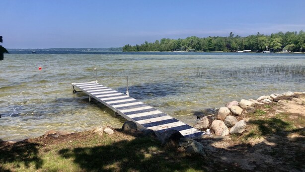 Un muelle de madera se adentra en un lago de aguas cristalinas, rodeado de rocas y hierba.