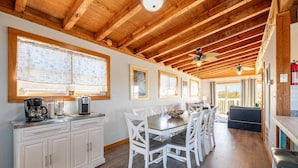 A spacious kitchen with wooden beams, white cabinets, and a dining area with white chairs. - Duck Life - Oceanside, Sound View, 325 Yards to Beach, Pool, Hot Tub, Tiki Bar, Pool Table, Pets OK (Duck)