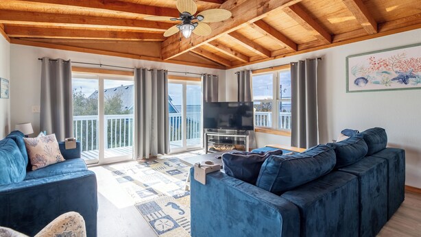A spacious living room with a wooden ceiling, a large TV, and a sofa set. - Duck Life - Oceanside, Sound View, 325 Yards to Beach, Pool, Hot Tub, Tiki Bar, Pool Table, Pets OK (Duck)