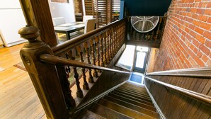 A wooden staircase with a metal handrail, leading to a room with a brick wall and a ceiling fan.