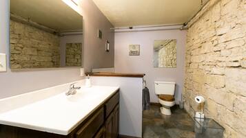 Un baño con pared de piedra, tocador de madera, lavabo blanco y un inodoro.