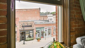 A window with a view of a brick building, a lamp on a table, and a curtain.