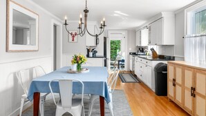 A modern kitchen with white cabinets, a dining area with a blue table and white chairs, and a chandelier.