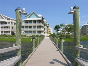 A wooden boardwalk leading to a waterfront property with multiple balconies and a green roof.