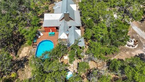 An aerial view of a house with a swimming pool, surrounded by dense greenery. - Secluded Cabin for 10 guests with Pool, Hot Tub, and Fire Pit (Wimberley)