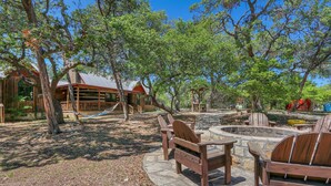 A rustic cabin with a wooden deck, surrounded by trees and a hammock. - Secluded Cabin for 10 guests with Pool, Hot Tub, and Fire Pit (Wimberley)