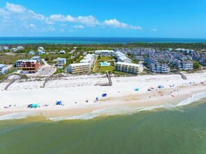 An aerial view of a coastal resort with beachfront properties, a boardwalk, and a clear view of the ocean.
