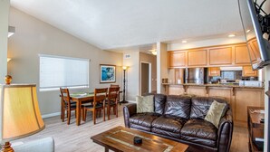 A living room with a leather sofa, a wooden coffee table, and a dining area with a table and chairs. - Cheery and bright upstairs unit is a perfect beach getaway! (Newport Beach)