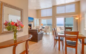 A spacious living room with a fireplace, a dining area with wooden furniture, and large windows offering ocean views.