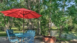 An outdoor patio with a red umbrella, blue metal chairs, and a brick fire pit. - Walk to Marina! Midway House by Sunbury Channel (Midway)
