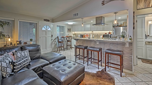 A spacious living room with a leather sofa, ottoman, and bar stools. A kitchen with a large island and stainless steel appliances is visible in the background. - 5 Mi to Dtwn: Austin Gem w/ Pool, Pets Welcome (Austin)