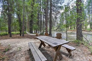 Une table de pique-nique avec des bancs, située dans une zone boisée près d’une rivière.