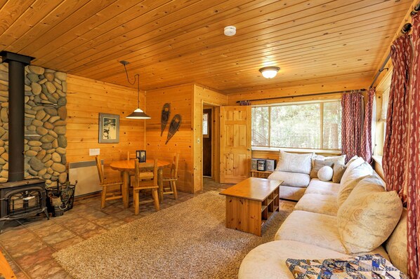 L’intérieur chaleureux d’un chalet avec une cheminée en pierre, des murs en bois, un coin repas et une grande fenêtre.