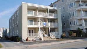 A multi-story residential building with balconies, a covered entrance, and a visible parking area. - Spacious, yet cozy 3 bedroom condo with free WiFi and a balcony located midtown on the ocean block just a short walk to the beach! (Ocean City)