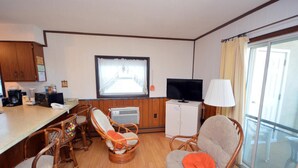 A compact hotel room with a kitchenette, a television, wicker chairs, and a large window. - Spacious, yet cozy 3 bedroom condo with free WiFi and a balcony located midtown on the ocean block just a short walk to the beach! (Ocean City)