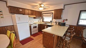 A compact kitchen with wooden cabinets, a refrigerator, stove, and a dining area with chairs. - Spacious, yet cozy 3 bedroom condo with free WiFi and a balcony located midtown on the ocean block just a short walk to the beach! (Ocean City)