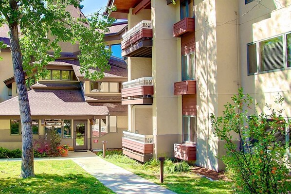A multi-story building with balconies, a visible entrance, and a well-maintained lawn.