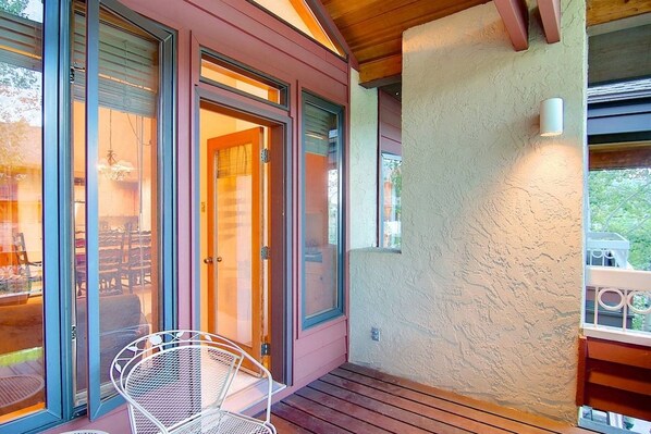 A covered outdoor area with a sliding glass door, a metal chair, and a wooden deck.