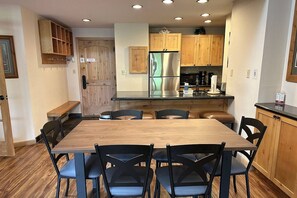 A modern kitchen with wooden cabinets, a stainless steel refrigerator, and a dining area with a wooden table and chairs.