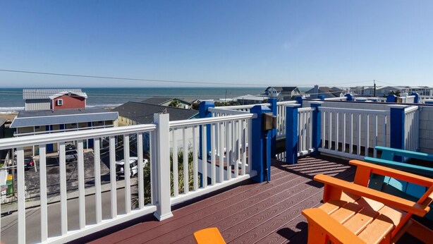 Eine Terrasse mit Blick auf das Meer, weiße Geländer und orangefarbene Stühle.
