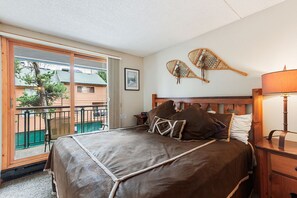 A bedroom with a large bed, a wooden headboard, a nightstand, a lamp, and a view of a balcony with a railing. - Breckenridge Ski-In/Ski-Out located in Downtown Breckenridge! Pool/Hot Tub Acces (Breckenridge)
