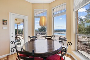 A dining area with a round table and chairs, large windows with blinds, and a view of the beach.