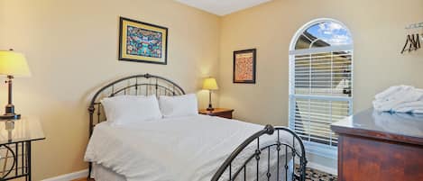 A bedroom with a bed, two bedside lamps, a wooden nightstand, a dresser, and a window with blinds.