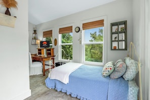 A bedroom with a bed, a desk, and a chair. There are windows with blinds, a clock, and a shelf with decorative items. - The Coop at Canyon Lake I Pool & Ideal for Families (Wimberley)