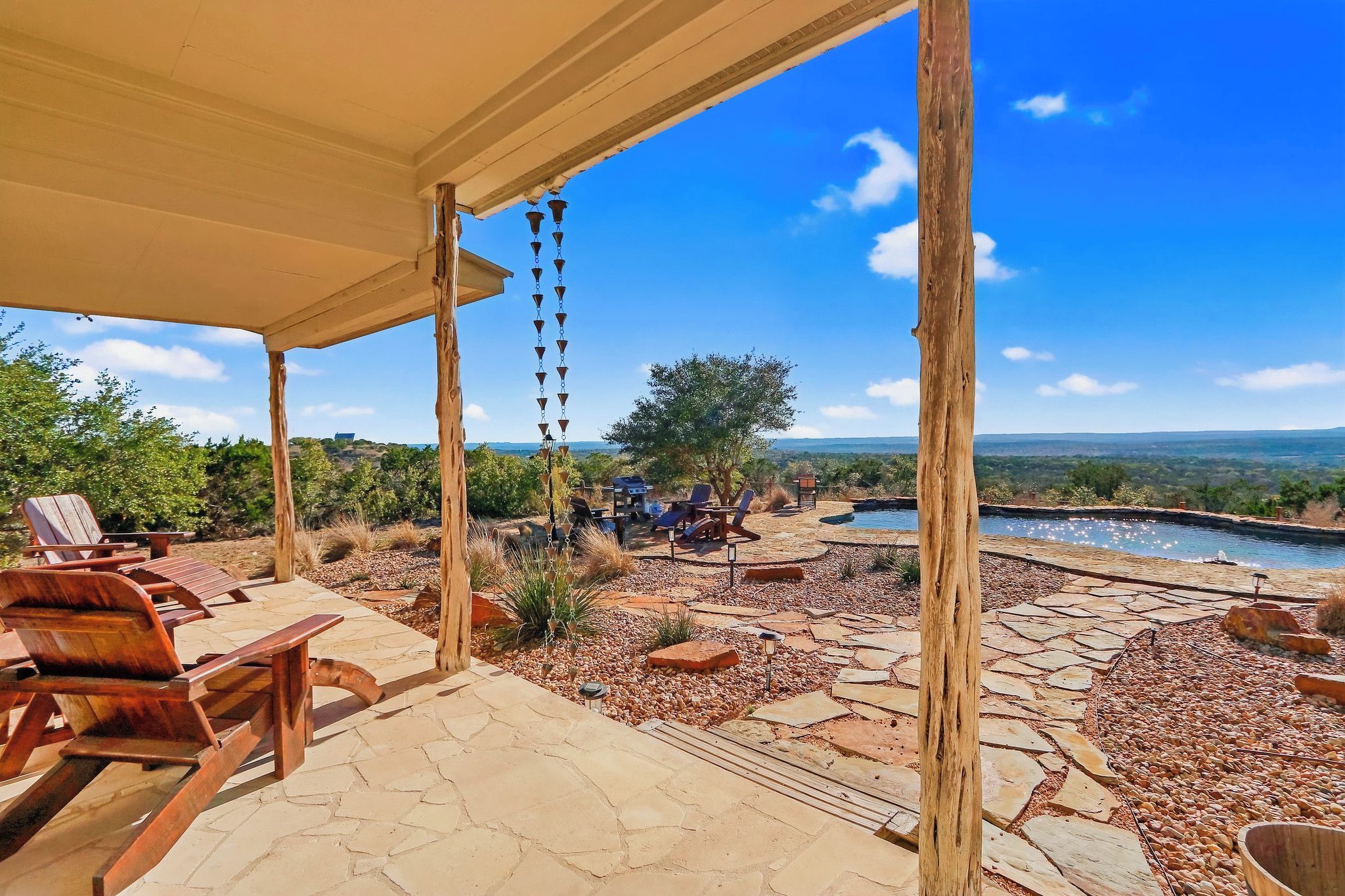 A covered outdoor seating area with wooden chairs and a stone patio.