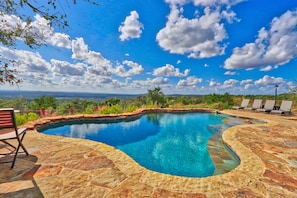 A swimming pool with a stone deck, surrounded by lounge chairs and a view of the landscape. - Soak in only the BEST Hill Country views form your own private pool! (Wimberley)