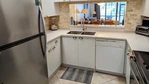 A modern kitchen with white cabinets, a stainless steel refrigerator, a built-in dishwasher, and a window with a view of the outdoors. - Beautiful 2/2 ground floor condo ⚓ resort style community (Bradenton)