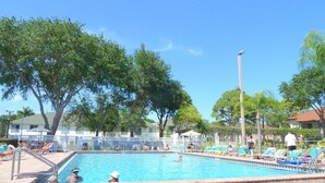 A swimming pool with lounge chairs and umbrellas, surrounded by trees and a fence. - Beautiful 2/2 ground floor condo ⚓ resort style community (Bradenton)