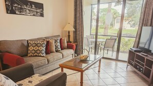 A living room with a sofa, a glass coffee table, a television, and a view of the outdoors. - Beautiful 2/2 ground floor condo ⚓ resort style community (Bradenton)
