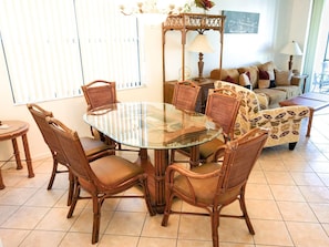 Un coin repas avec une table à plateau de verre entourée de chaises en osier, un canapé agrémenté de coussins à motifs et une lampe posée sur une table d’appoint.