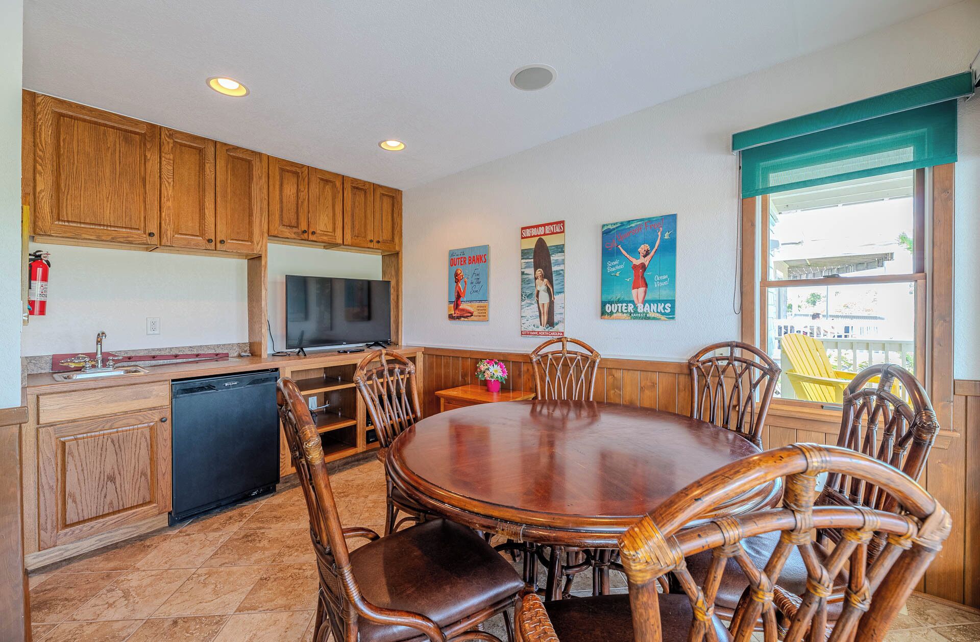 A kitchen with wooden cabinets, a built-in dishwasher, a dining table with chairs, and a large window with a view.