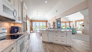A spacious kitchen with a large island, wooden flooring, and a view to a balcony. - Terning Point - Corolla, Crown Point, Oceanfront, 20 Yds to Beach, Pool, Hot Tub, Pets OK (Corolla)