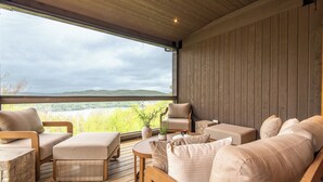 Una zona de estar al aire libre acogedora con terraza de madera, asientos acolchados y vistas a un paisaje natural.