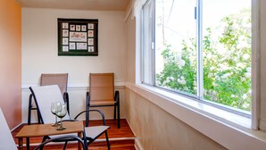 Ein Eckzimmer mit Fenster, ein gerahmtes Bild an der Wand und ein Tisch mit zwei Stühlen sowie einem Weinglas.